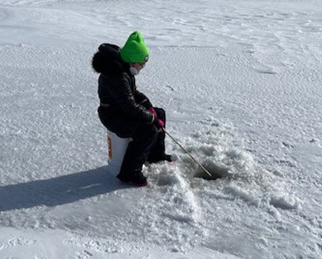 A child ice fishing on a frozen lake as part of a traditional outdoor learning activity.